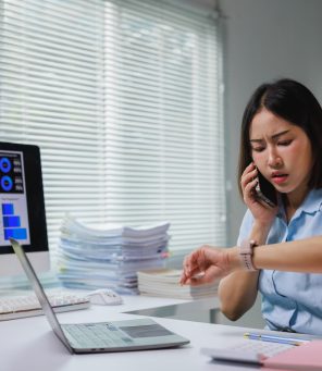 Asian businesswoman stressed by overwhelming work, checking time and talking on phone